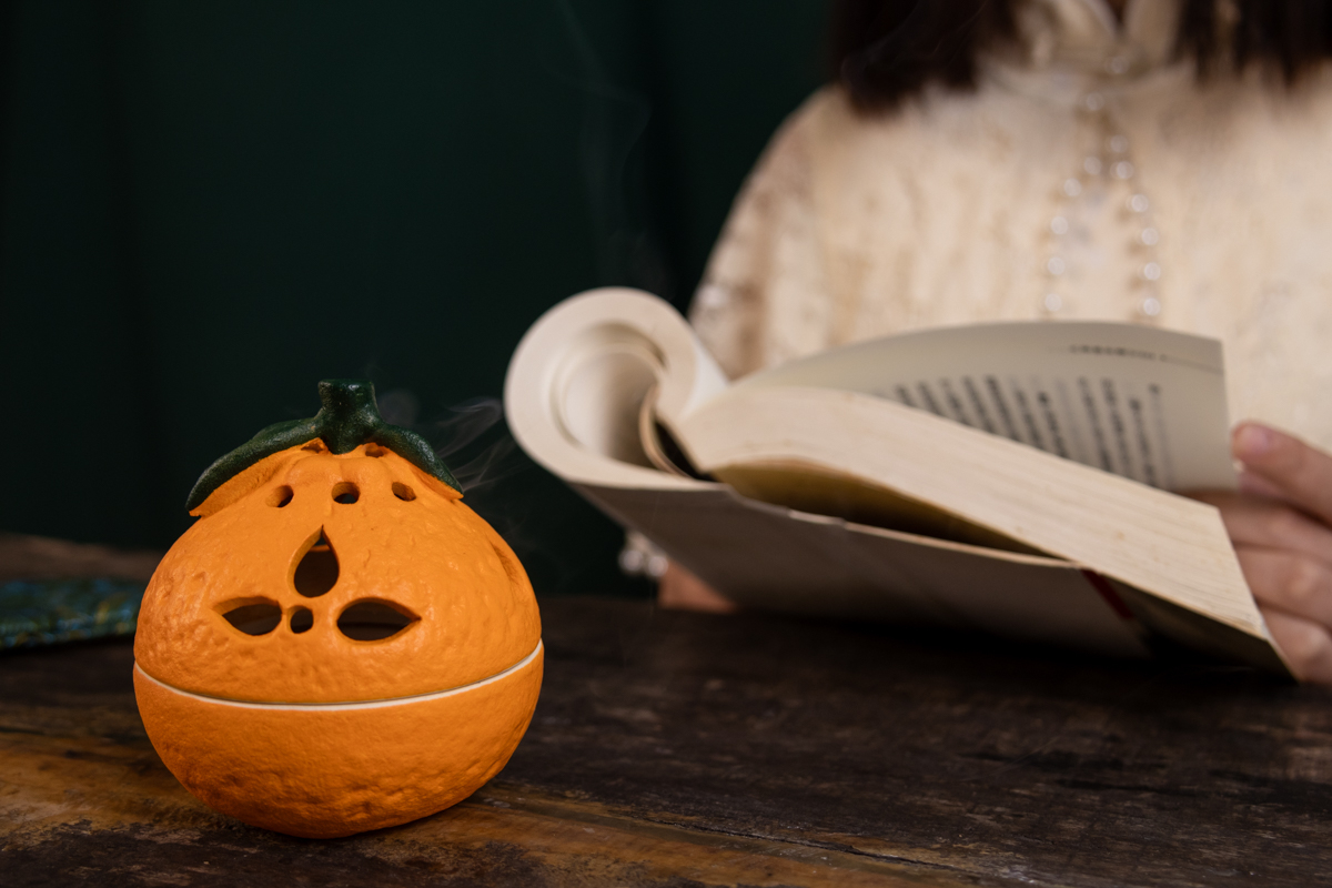 A ceramic pumpkin shaped candle holder with a book in the backgroundDescription automatically generated