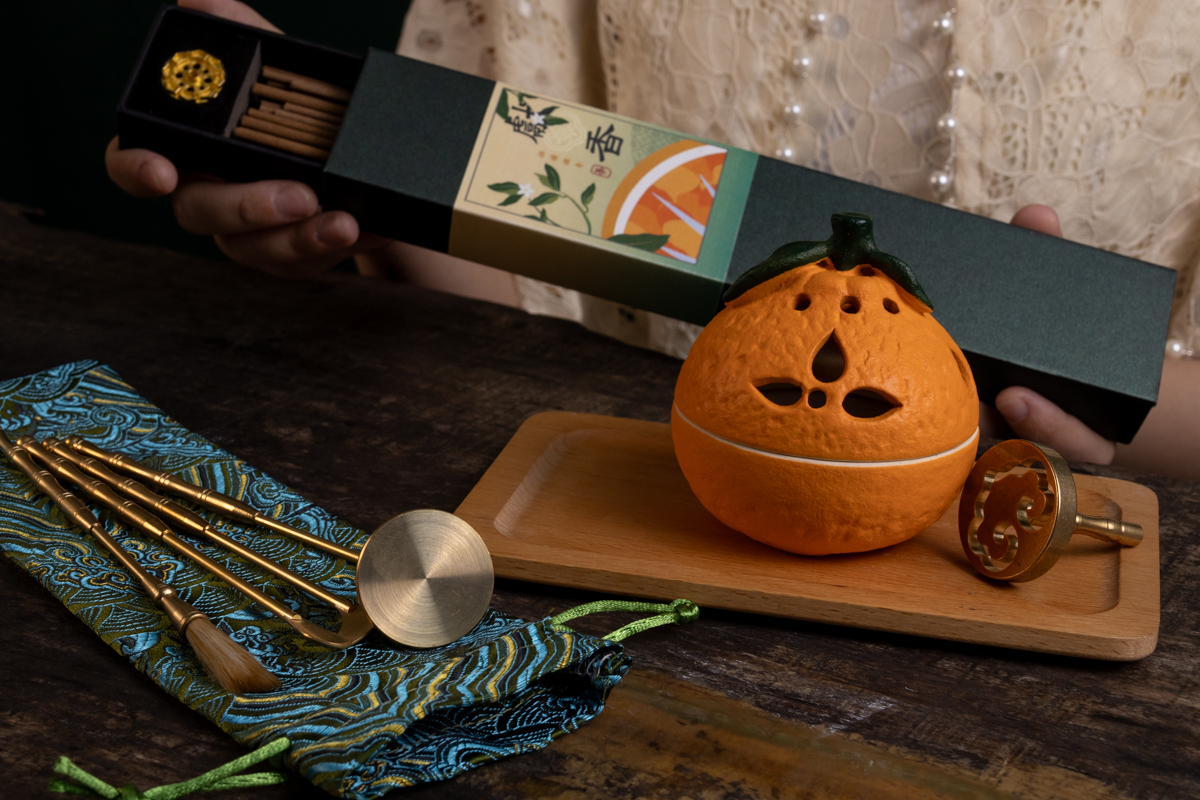 A ceramic pumpkin shaped candle holder with a book in the backgroundDescription automatically generated